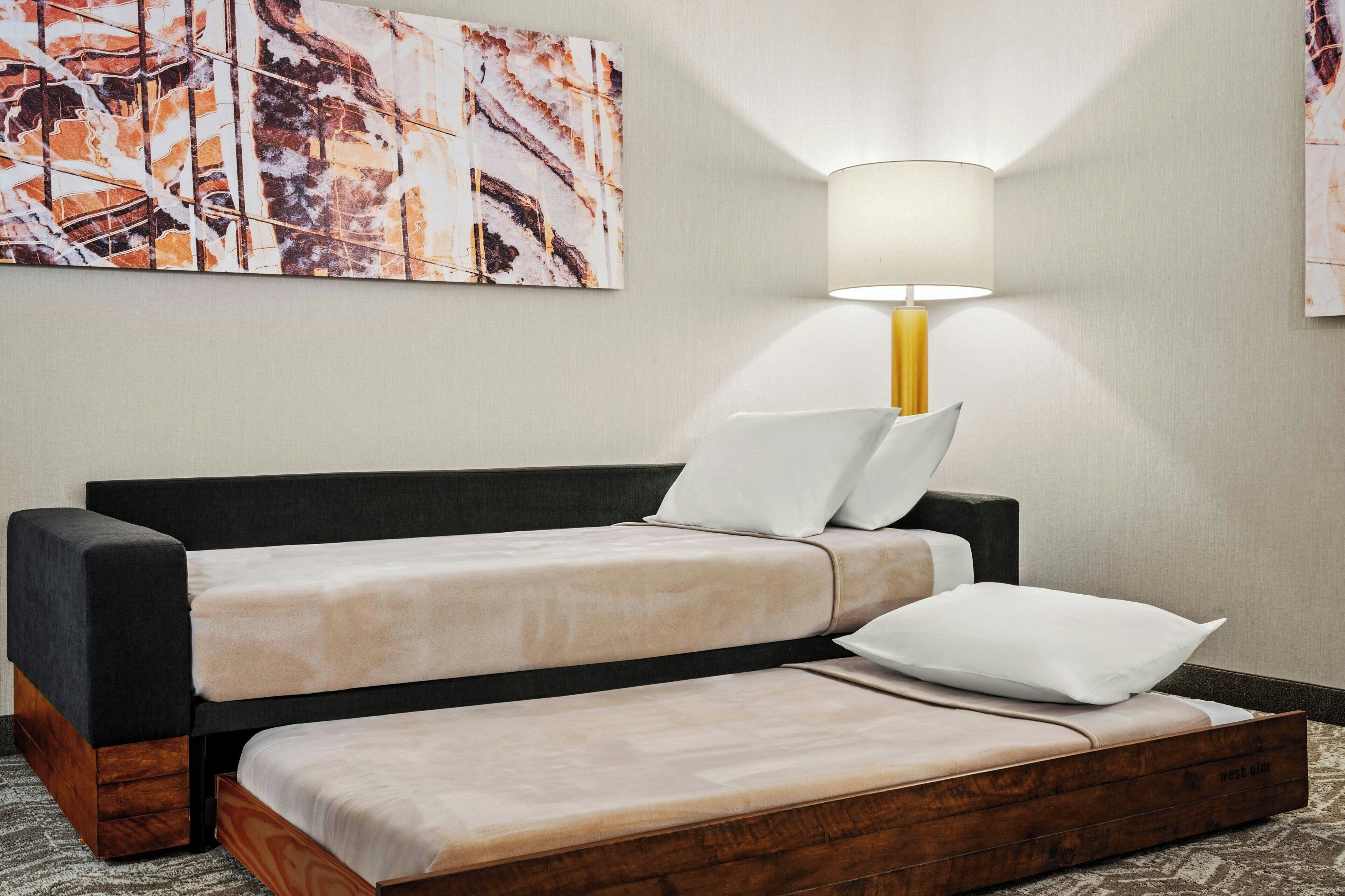 Una habitación de hotel moderna con una cama plegable, una mesita de noche y una lámpara.