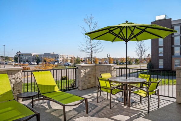 A patio with green chairs and a table, a green umbrella, and a view of a parking lot and buildings.