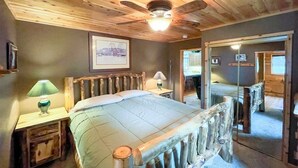 A wooden-paneled bedroom with a bed, two bedside lamps, a ceiling fan, and a framed picture on the wall. - Round Lake Retreat for All Seasons (Park Falls)