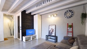 A modern living room with a grey sofa, a flat-screen TV, a clock, and a sign that reads "PEACE & LOVE".