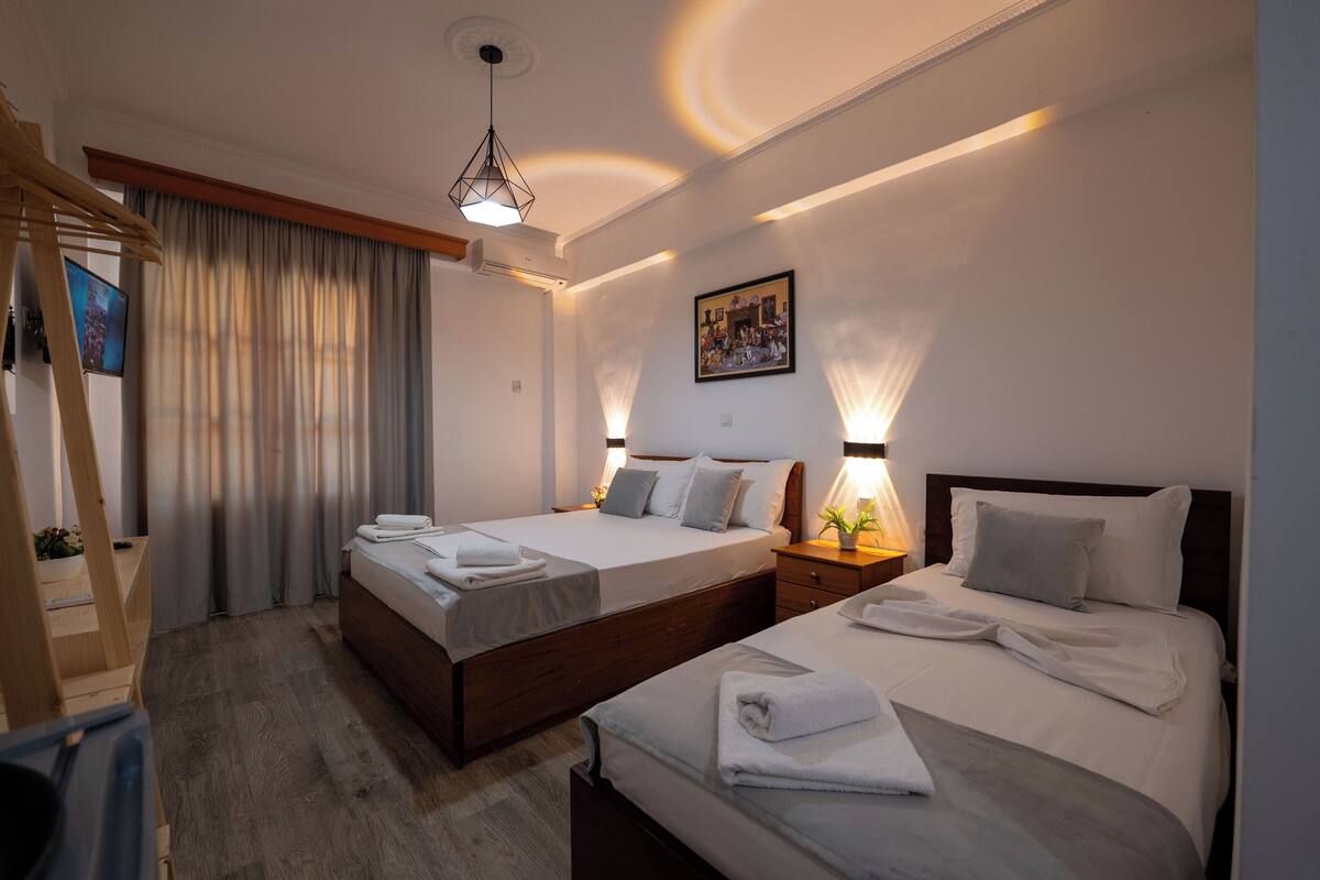 A hotel room with two beds, a wooden desk, a TV, and a painting on the wall.