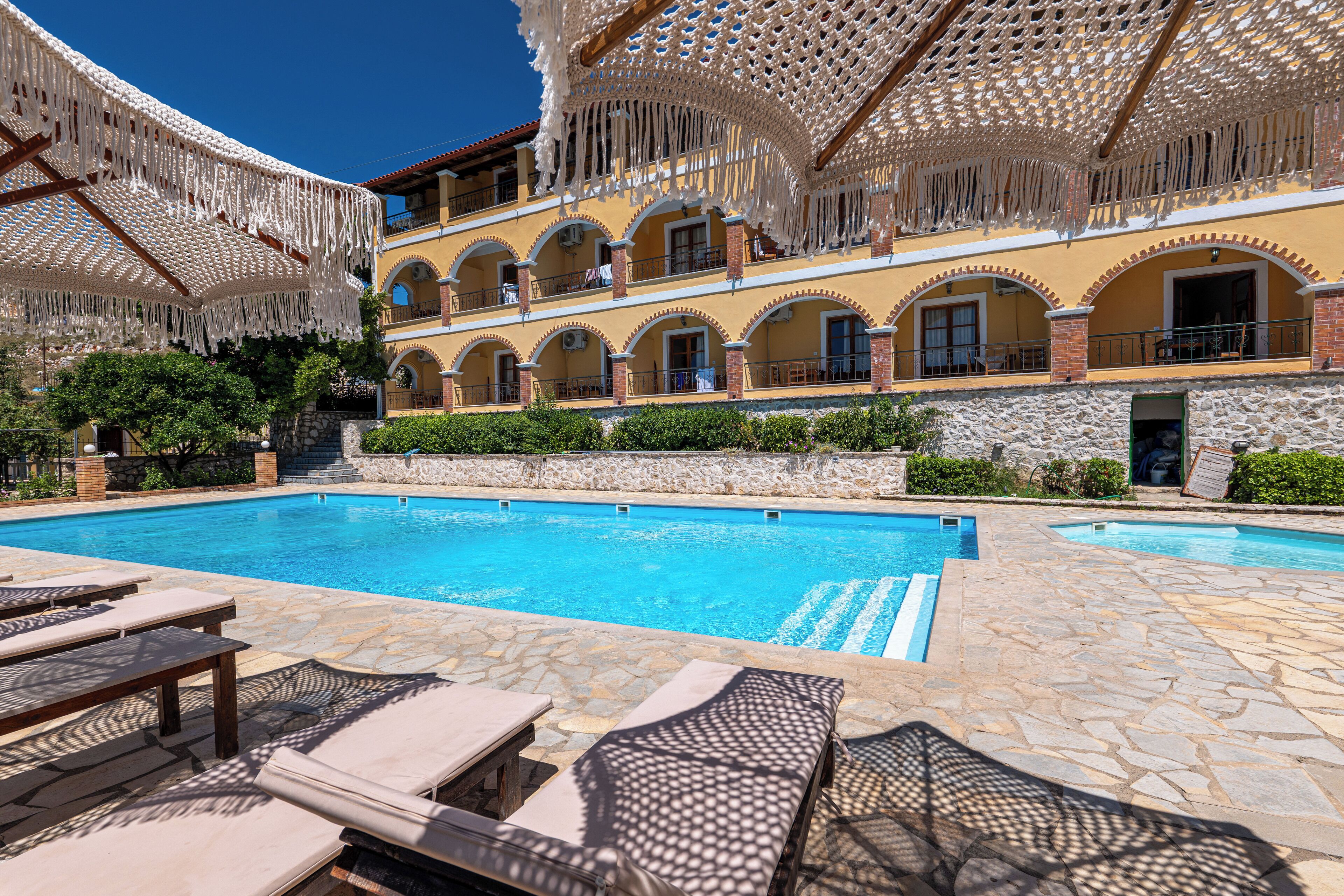 A pool area with lounge chairs, a stone pool, and a building with arched balconies.