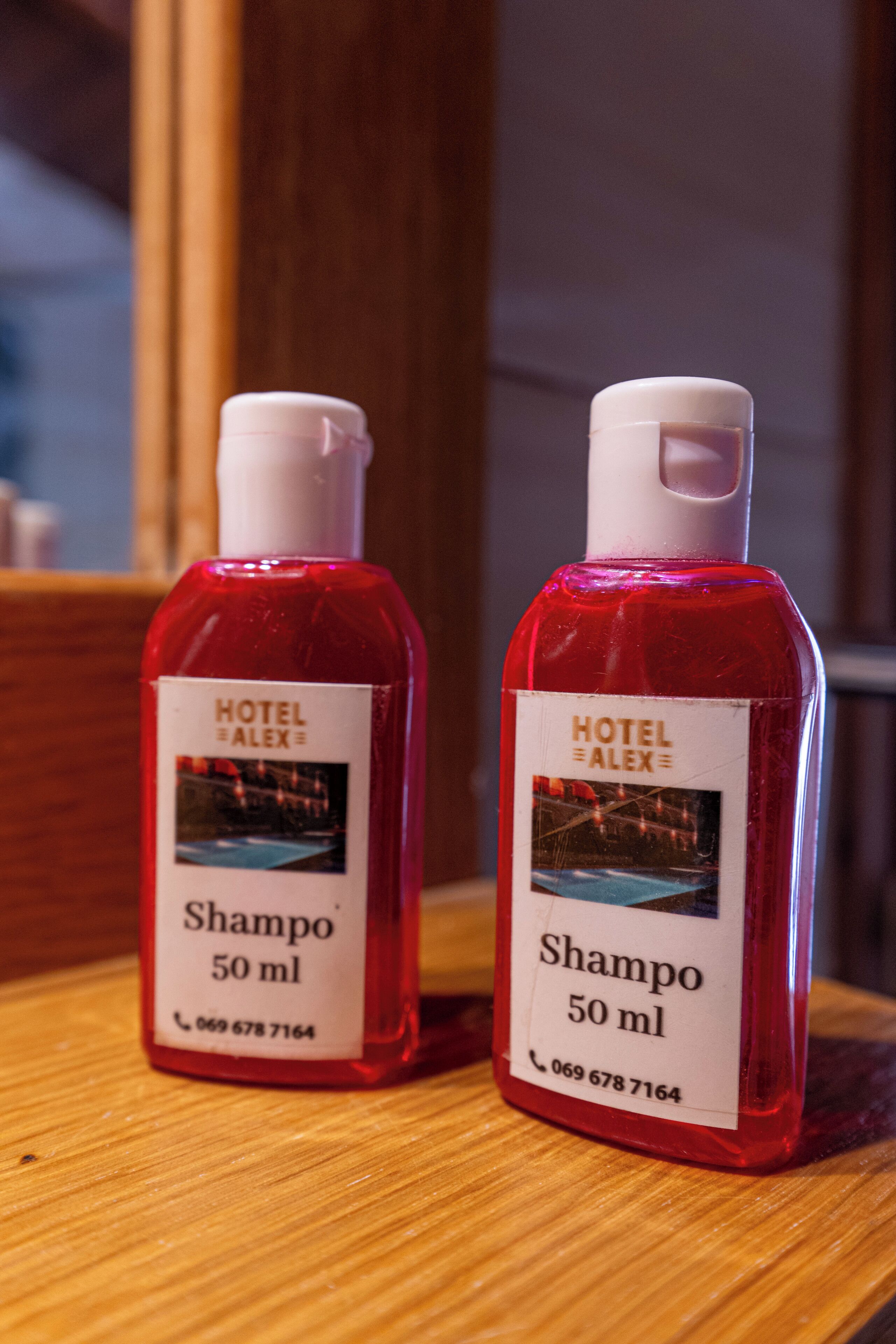 To røde shampoo flasker med hvide etiketter står på en træoverflade.