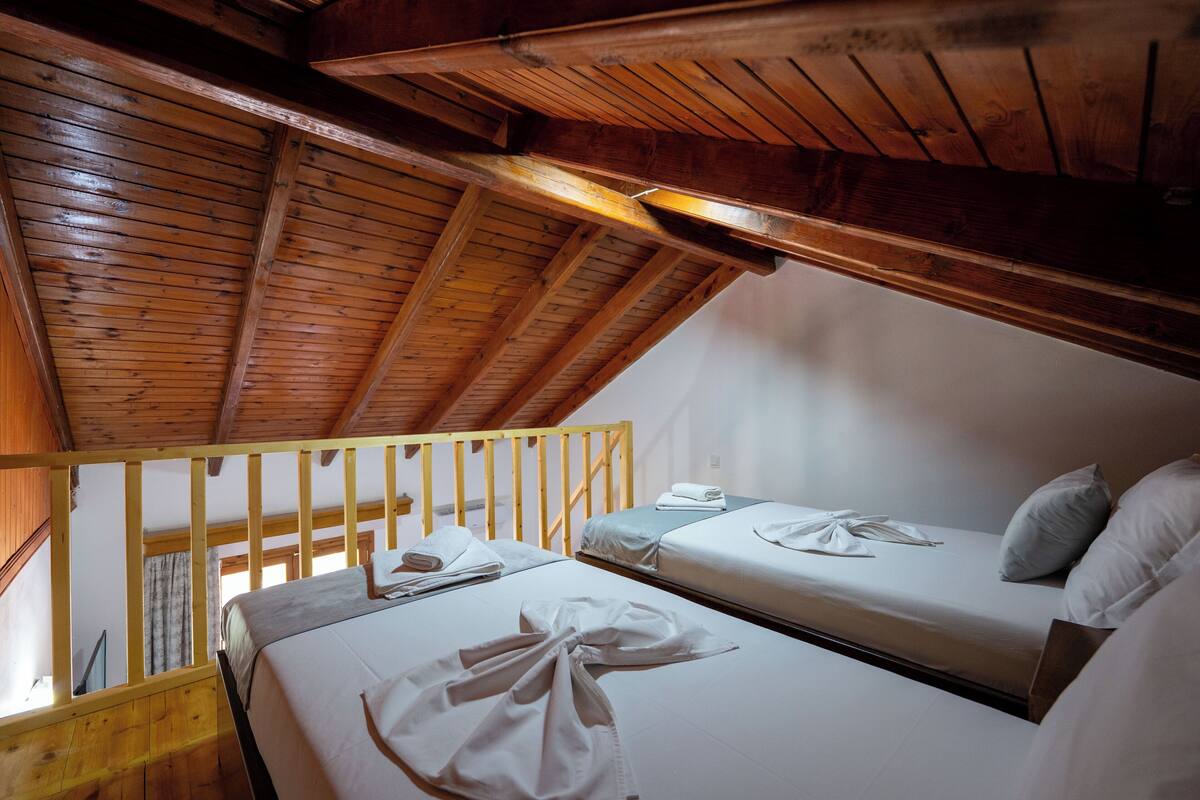 A room with two beds, wooden beams, and a sloped ceiling.