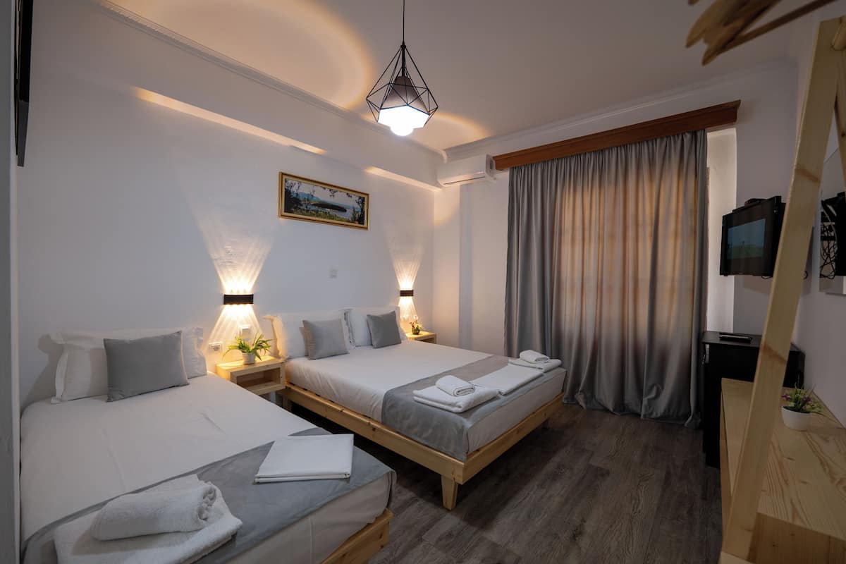 A hotel room with two beds, a wooden floor, a painting on the wall, and a television on a stand.