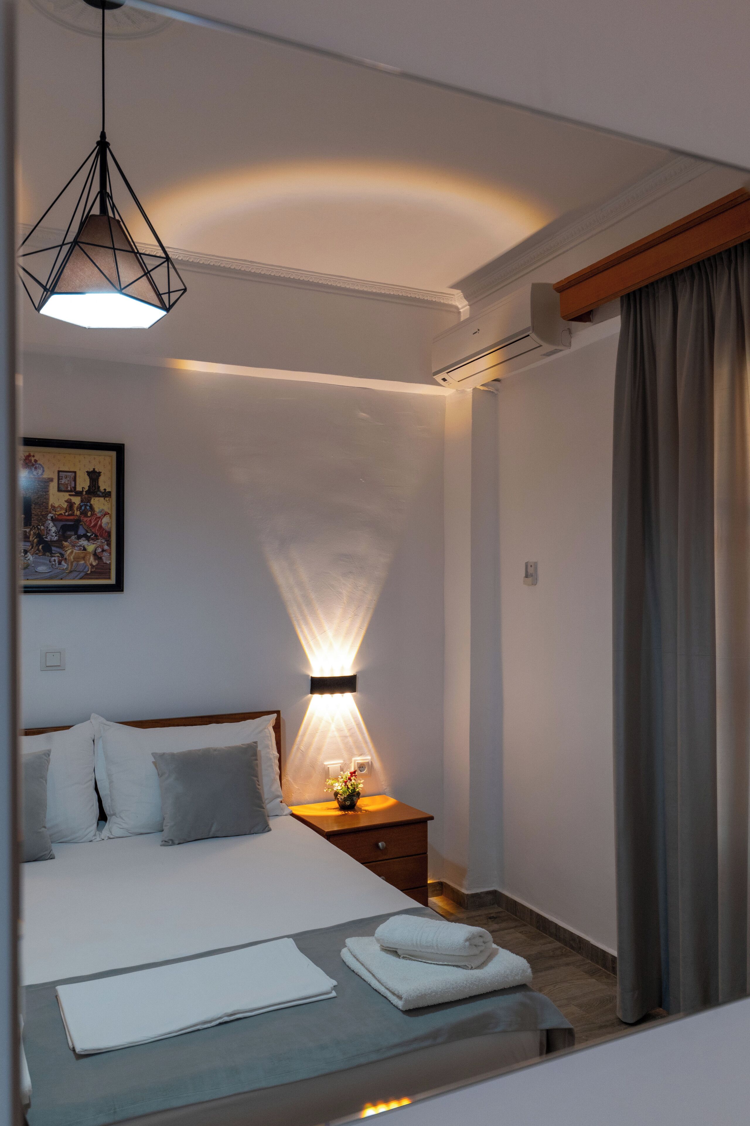 A hotel room with a neatly made bed, a bedside lamp, a framed picture on the wall, and a window with curtains.
