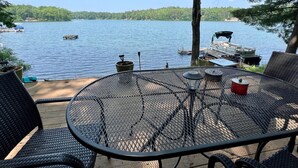 A patio with a round metal table and chairs, overlooking a lake with boats and docked at the shore.