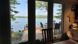 A room with large windows overlooking a lake, a wooden deck, and outdoor furniture.