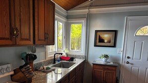 A kitchen with wooden cabinets, a stove, a sink, and a window with a view of trees.