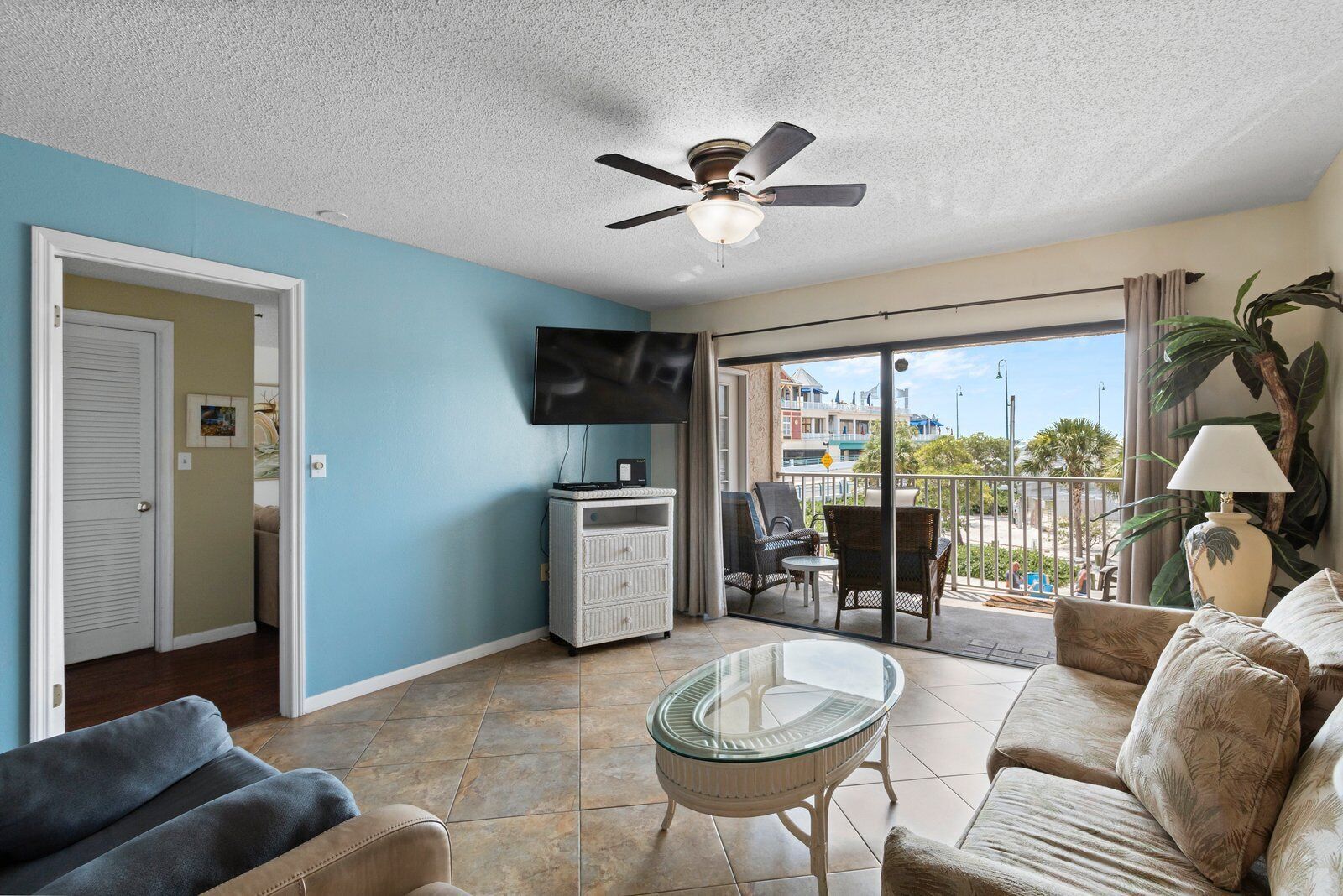 A living room with a flat-screen TV, a ceiling fan, a glass coffee table, and a sofa.