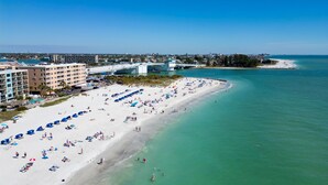 A beach with numerous umbrellas and people, a bridge, and buildings in the background. - Top Floor at Johns Pass | BP #502 (Madeira Beach)