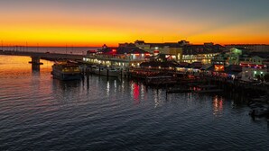 A waterfront hotel with a pier extending into the water, featuring multiple dining establishments and a view of the sunset. - Top Floor at Johns Pass | BP #502 (Madeira Beach)