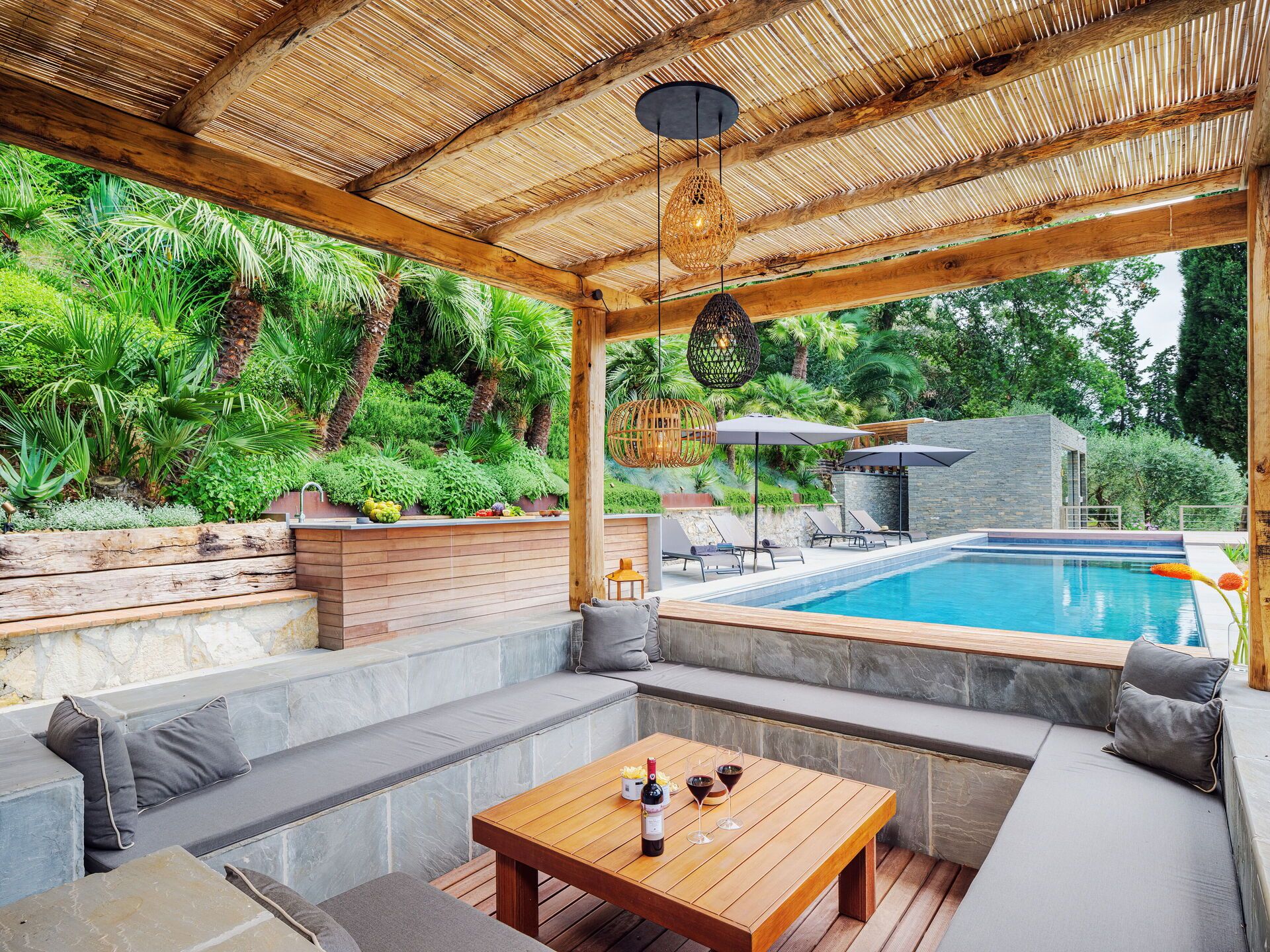 An outdoor seating area with a pool, wooden furniture, and a thatched roof.
