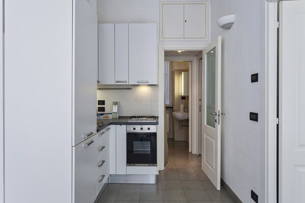 A narrow kitchen with white cabinets, a stove, and a sink. - A Un Passo dalla Spiaggia di Camogli by Wonderful Italy (Camogli)