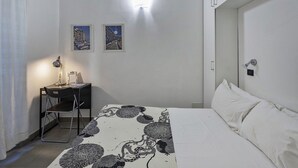 Ein Schlafzimmer mit einem Bett, einem Schreibtisch mit Stuhl, zwei gerahmten Bildern an der Wand und einem Nachttisch.