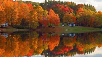 Un chalet au bord du lac, dont l’image se reflète dans l’eau, entouré d’arbres aux couleurs automnales.