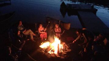 A group of people gathered around a campfire on a dock by a body of water at night.