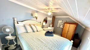 A bedroom with a bed, a bedside fan, a ceiling fan, a mirror, a wooden wardrobe, and a wall with a framed picture. - Lake Demmon Lodge-Beach,Boats,Fishing,FUN!! (Bath)