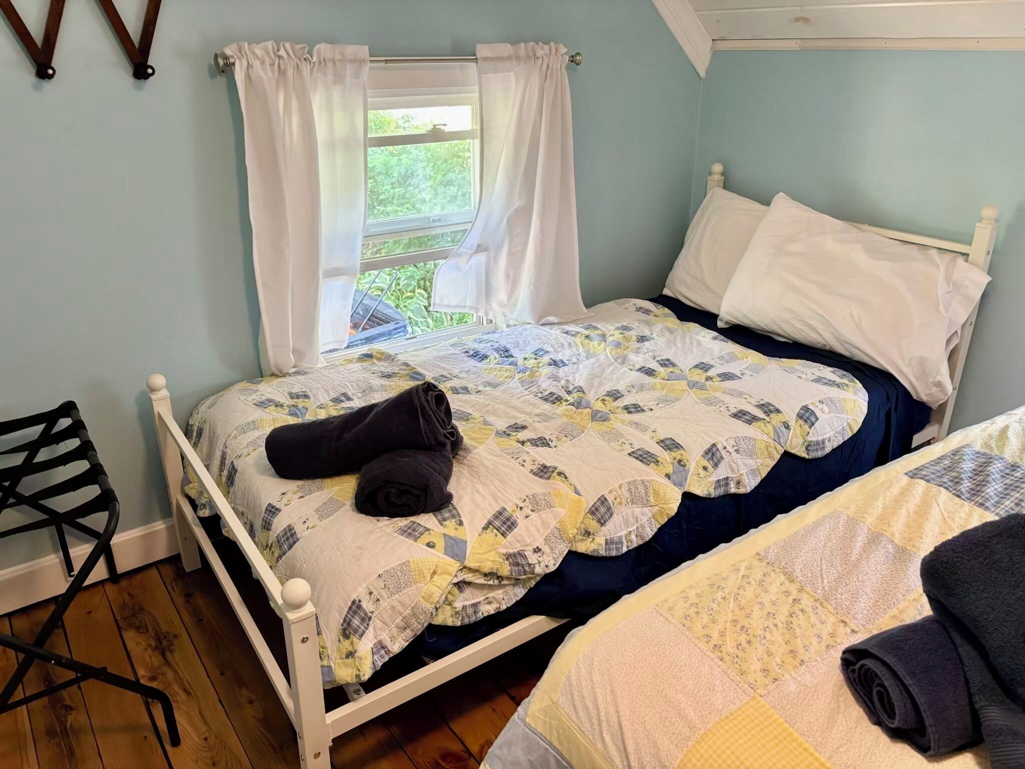 Uma cama de solteiro com um edredom, uma cadeira e uma janela com cortinas.
