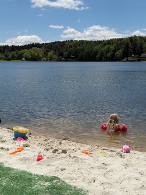 A lake with a sandy beach, a child playing in the water, and a forest in the background. - Lake Demmon Lodge-Beach,Boats,Fishing,FUN!! (Bath)