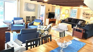 A spacious living room with a wooden dining table, blue armchairs, a black sofa, and a TV. - Lake Demmon Lodge-Beach,Boats,Fishing,FUN!! (Bath)