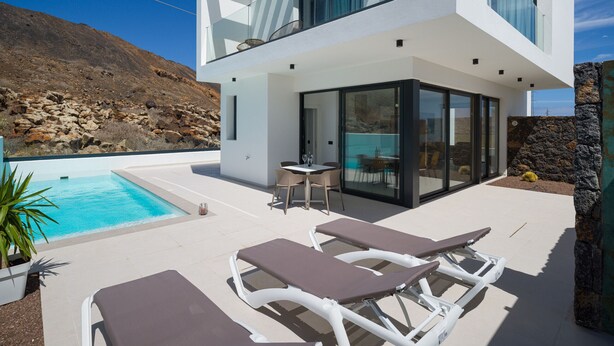 Et moderne hus med to etager, en pool, udendørs møbler og udsigt til det klippefyldte landskab.