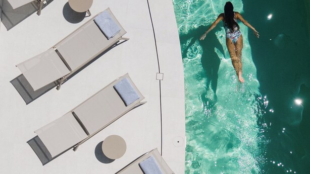 A poolside area with lounge chairs and a person swimming. - Anapollo Boutique Hotel - Adults Only (Naxos)