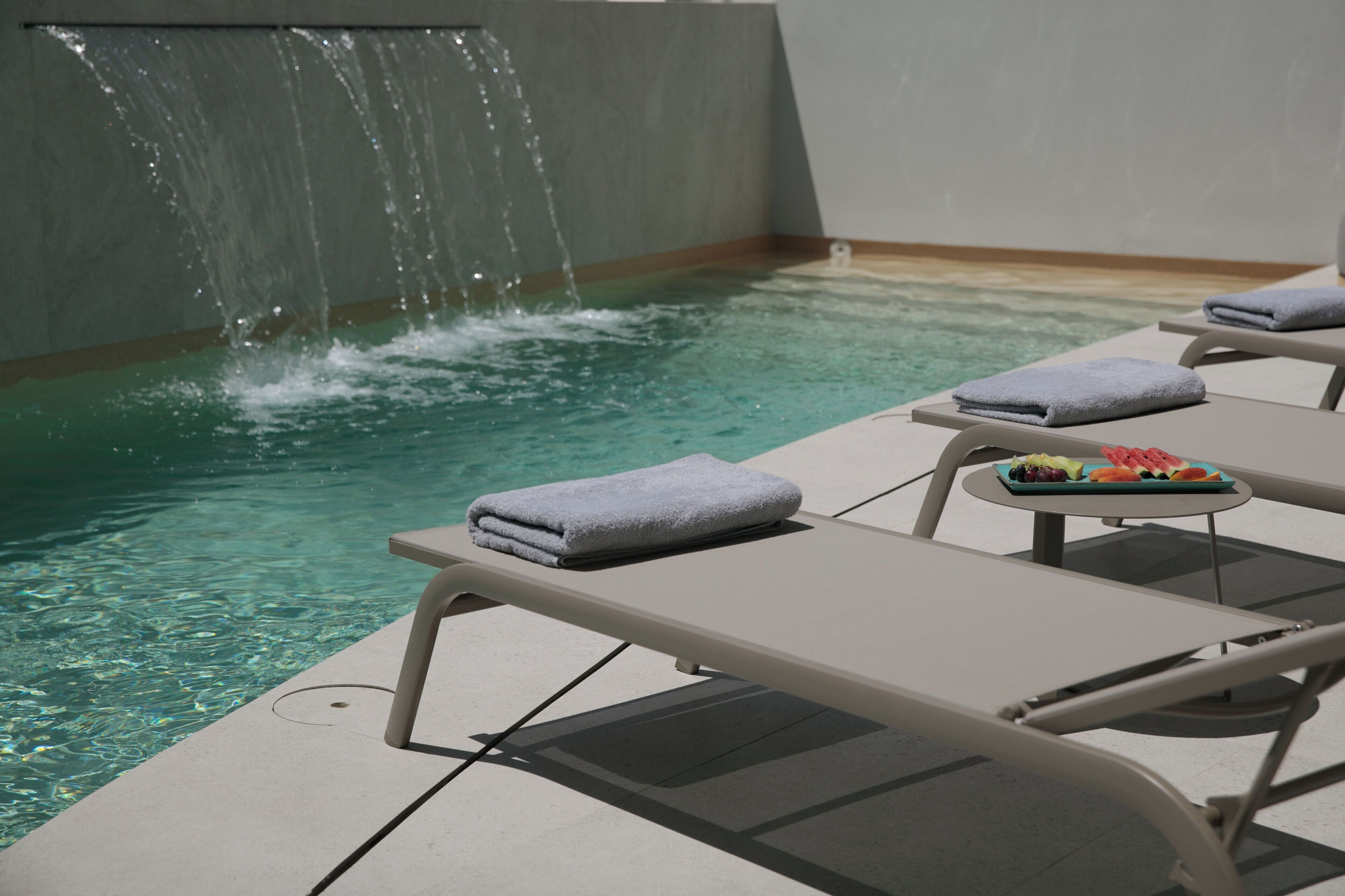 A poolside area with lounge chairs and a small table with towels and fruit.