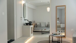 A modern, well-lit living room with a sofa, coffee table, and a round rug. A mirror and pendant lights are visible. - Anapollo Boutique Hotel - Adults Only (Naxos)
