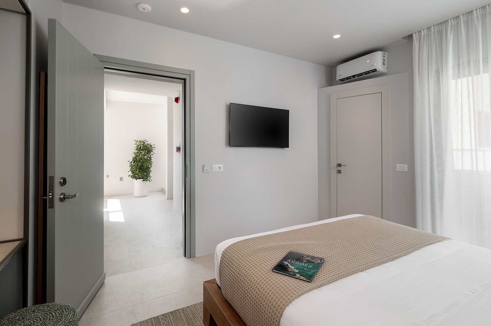 Une chambre d’hôtel équipée d’un lit, d’un téléviseur à écran plat fixé au mur, d’une porte donnant sur un couloir et d’un appareil de climatisation mural.