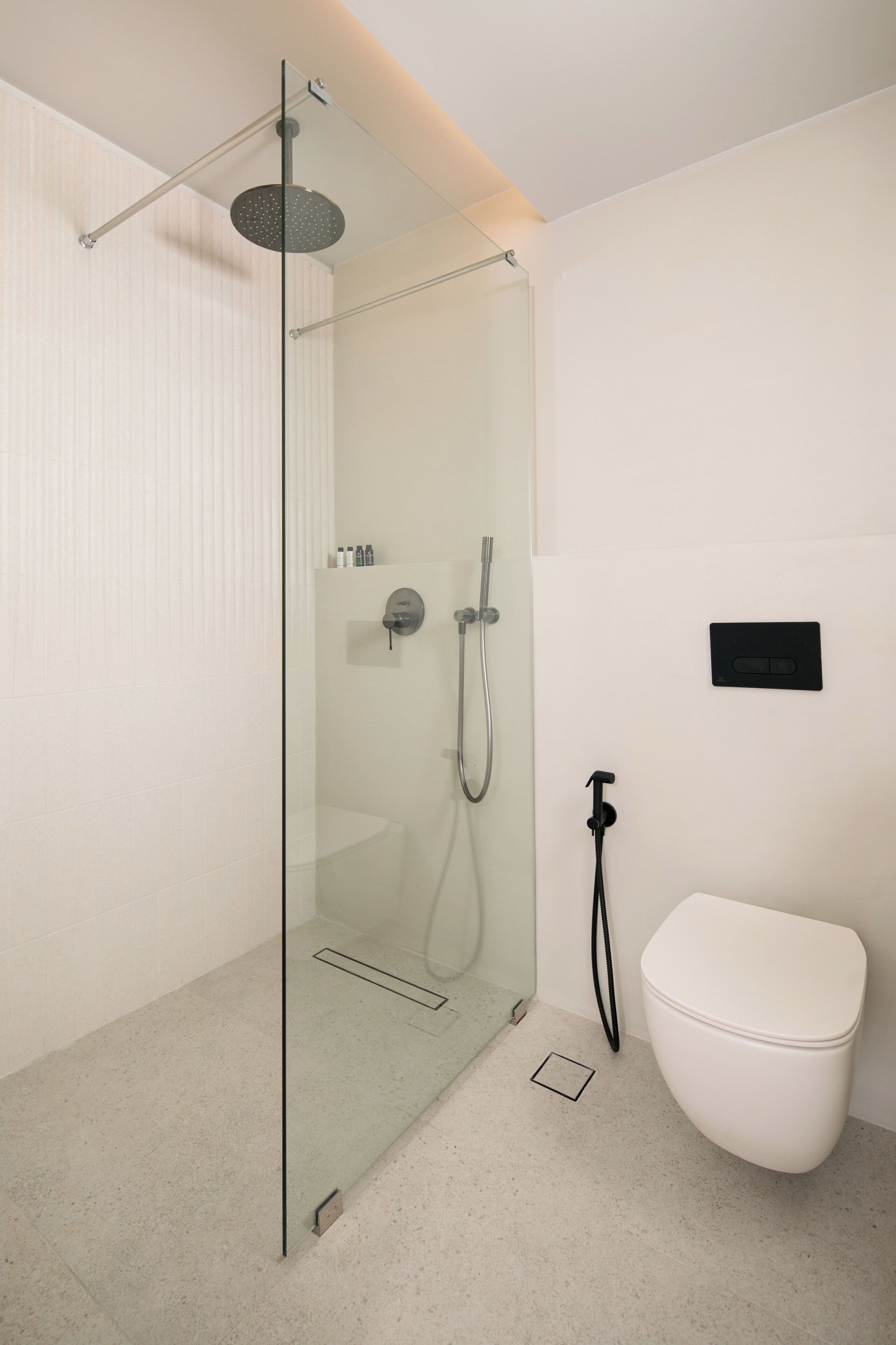 Une salle de bain moderne avec une douche à parois de verre, des toilettes blanches et un robinet fixé au mur.