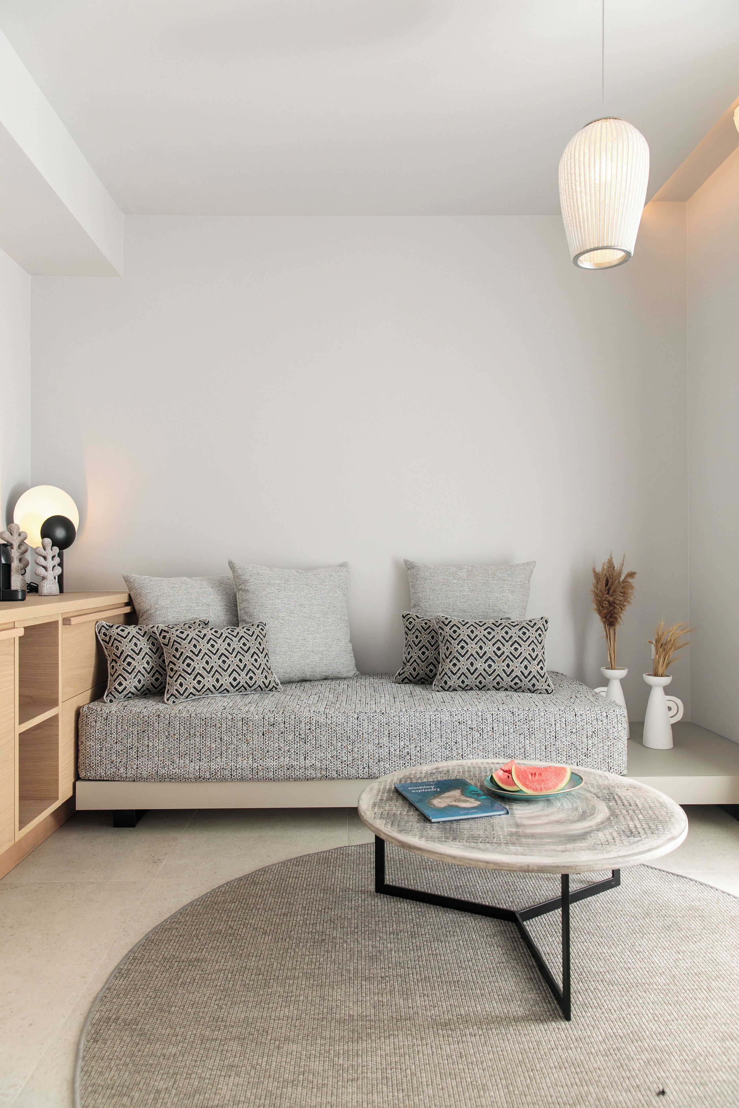 A modern living room with a sofa, a round coffee table, and a hanging light fixture.