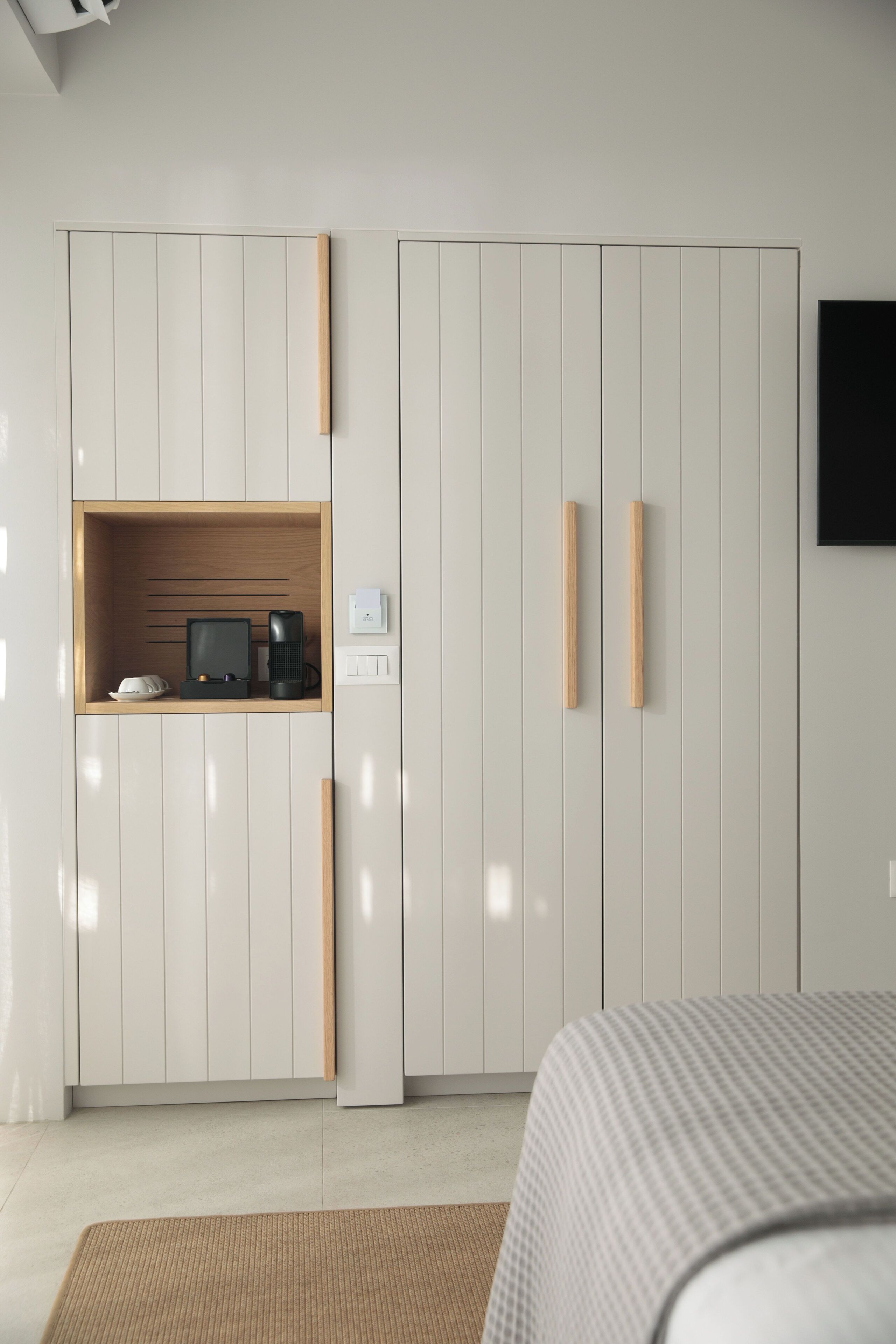 Quarto com cama, guarda-roupa com prateleira embutida e televisão na parede.