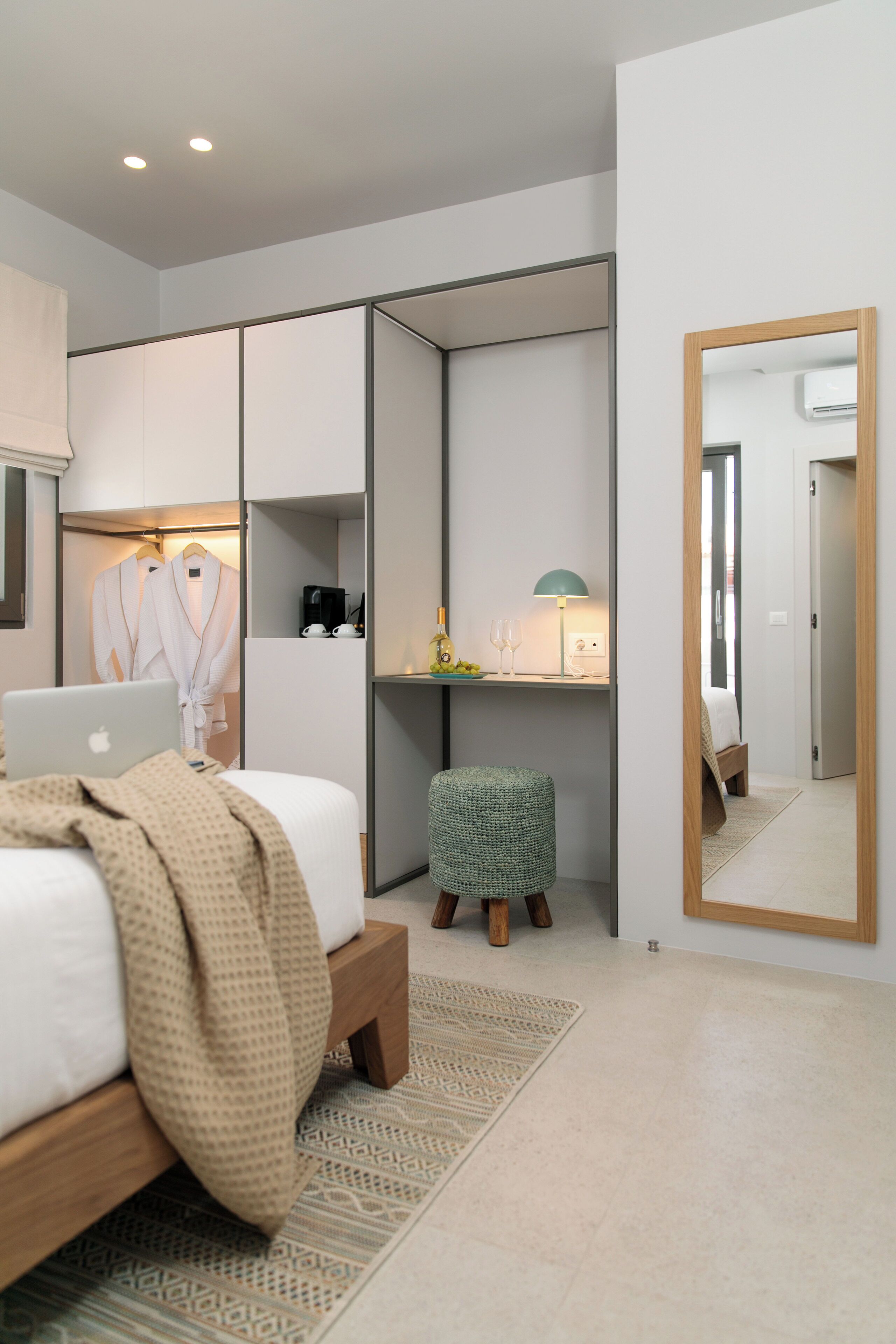 Ett modernt hotellrum med en säng, ett skrivbord med en bärbar dator, en spegel och en garderob.