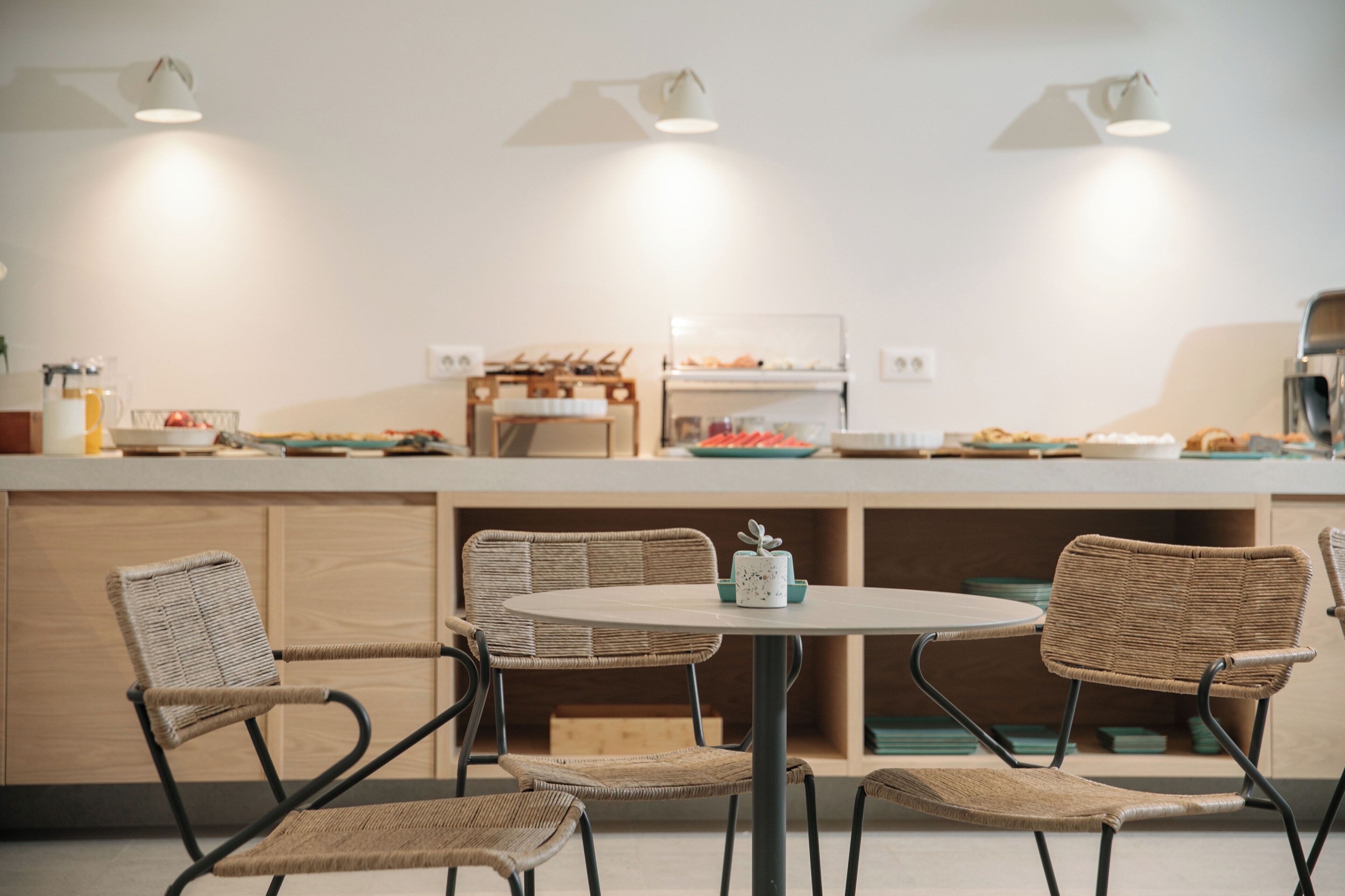 A modern kitchen with a round dining table, wicker chairs, and a buffet counter with food items.