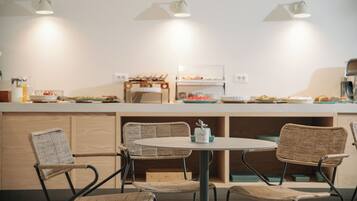 A modern kitchen with a round dining table, wicker chairs, and a buffet counter with food items.