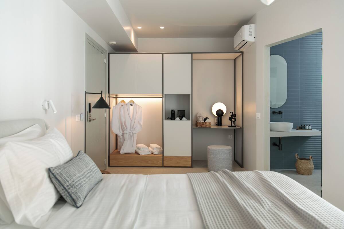 Un dormitorio moderno con una cama grande, un vestidor, un baño con un espejo amplio y un pequeño espacio de descanso.