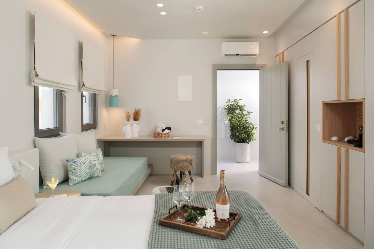 Una habitación de hotel moderna con una cama, una mesita de noche y un espacio de escritorio. Hay una botella de vino y copas sobre una bandeja en la cama.