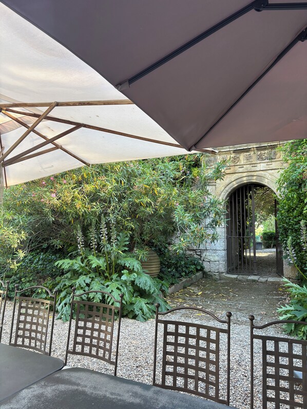 Un patio al aire libre con un arco de piedra, una pérgola que da sombra y un camino de grava.