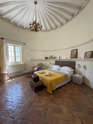 Un dormitorio con cama, una silla, una mesa, un radiador y una ventana.