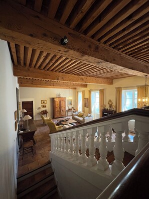 Un vaste salon dotĂ© dâun haut plafond en bois, dâun escalier avec des balustrades blanches et dâune vue sur la salle Ă manger adjacente.