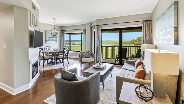 Een ruime woonkamer met een grote schuifpui die leidt naar een balkon met uitzicht op een golfbaan.