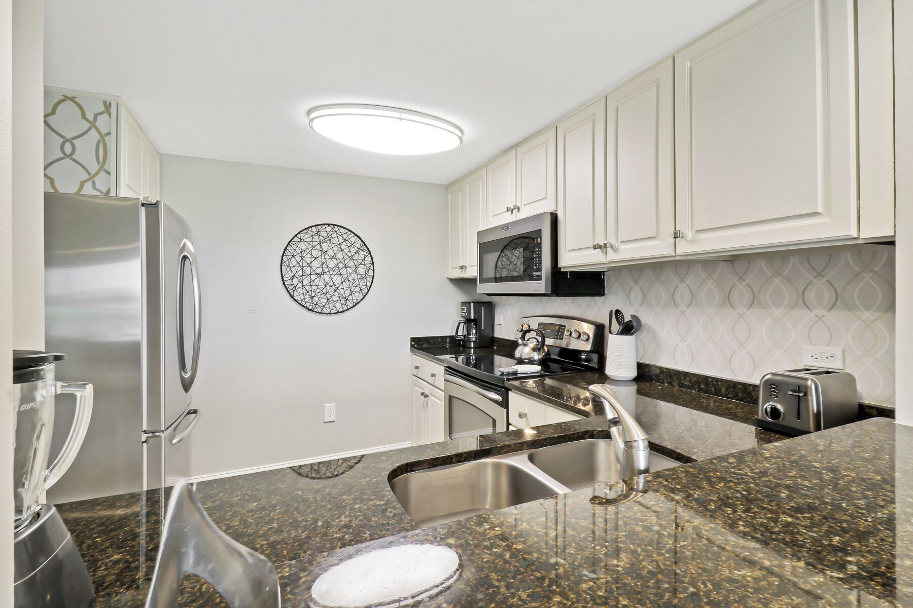 A modern kitchen with white cabinets, stainless steel appliances, a granite countertop, and a decorative wall piece.