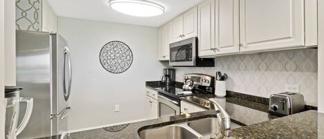A modern kitchen with white cabinets, stainless steel appliances, a granite countertop, and a decorative wall piece.