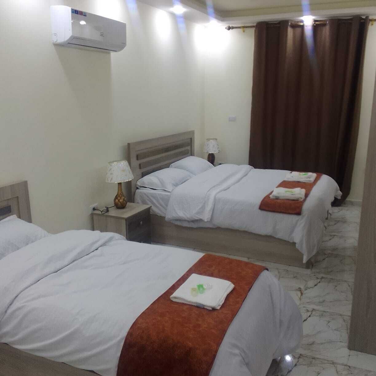Habitació d'hotel amb dos llits, una tauleta de nit amb una làmpada, un aparell d'aire condicionat i una cortina.