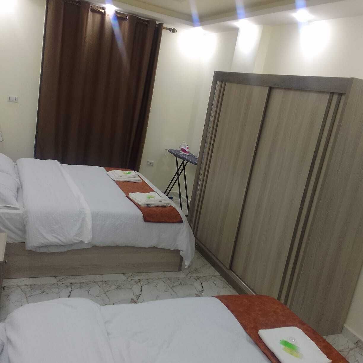 A hotel room with two beds, a small table with an ironing board, and a wardrobe.
