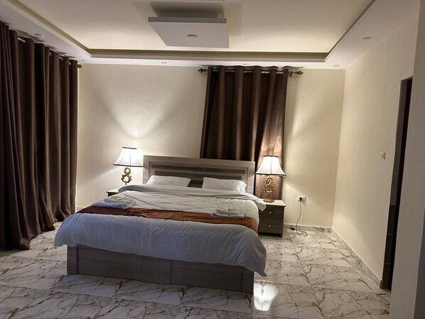 Una habitación de hotel con cama, mesitas de noche, una lámpara y cortinas.