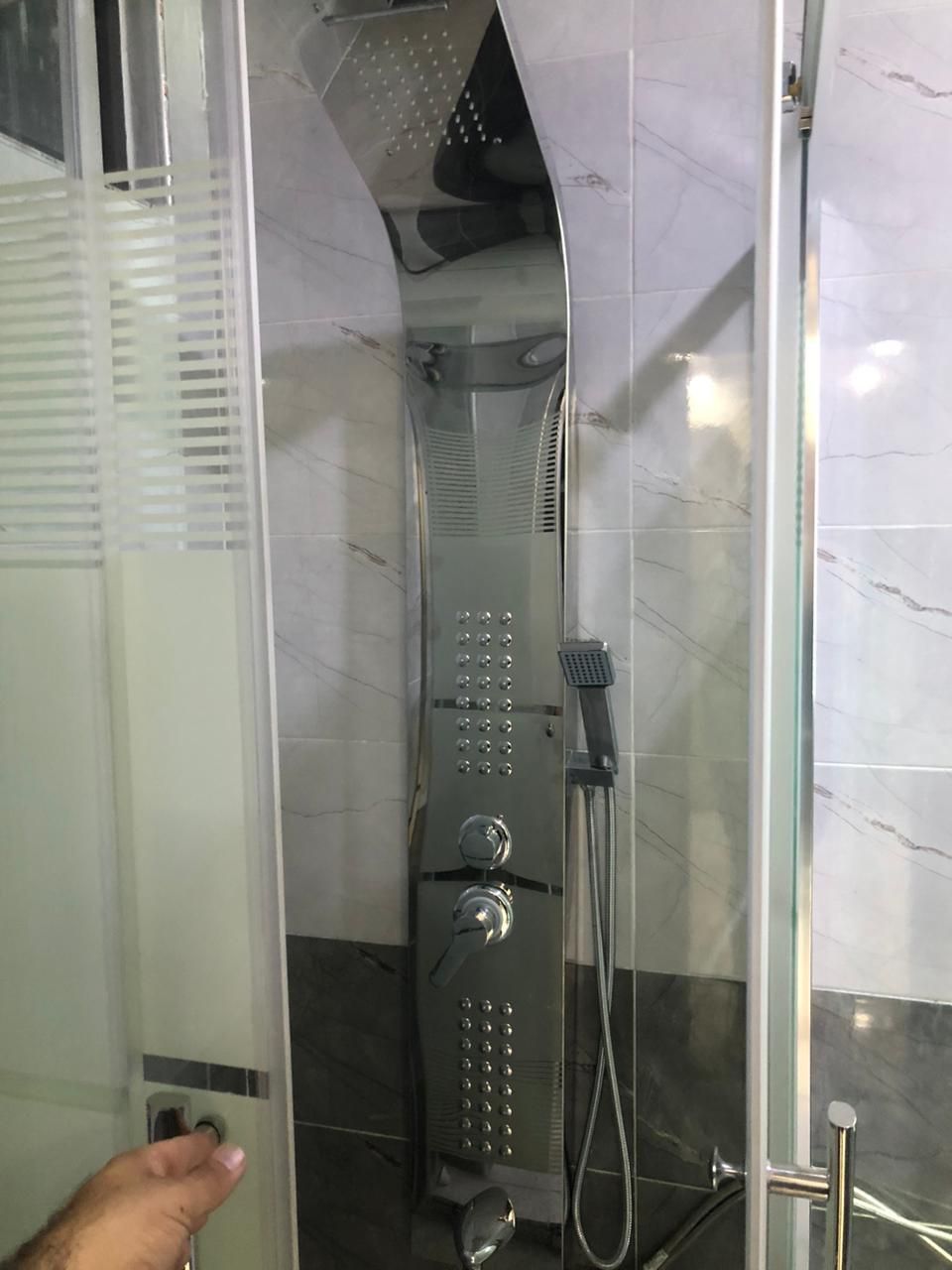 A glass-enclosed shower stall with a handheld showerhead and a handheld faucet.