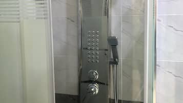 A glass-enclosed shower stall with a handheld showerhead and a handheld faucet.