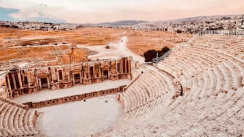 An ancient amphitheater with tiered seating and a central stage, surrounded by ruins.